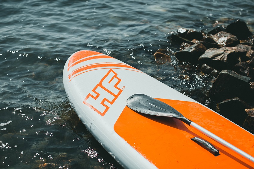 A white and orange inflatable SUP with a paddle on the water