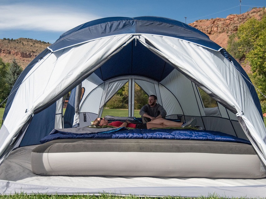 A man and a woman relax inside the spacious Ozark Trail 10 Person 3 Room Tent