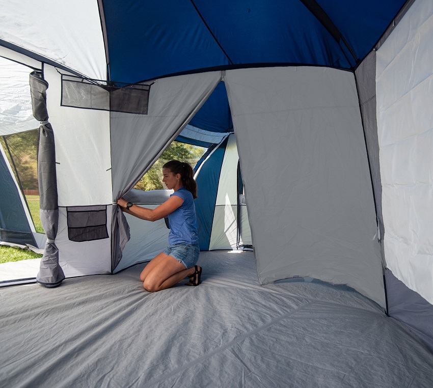 A woman straps the room divider inside the Ozark Trail Hazel Creek 20-Person Star Tent with Screen Room