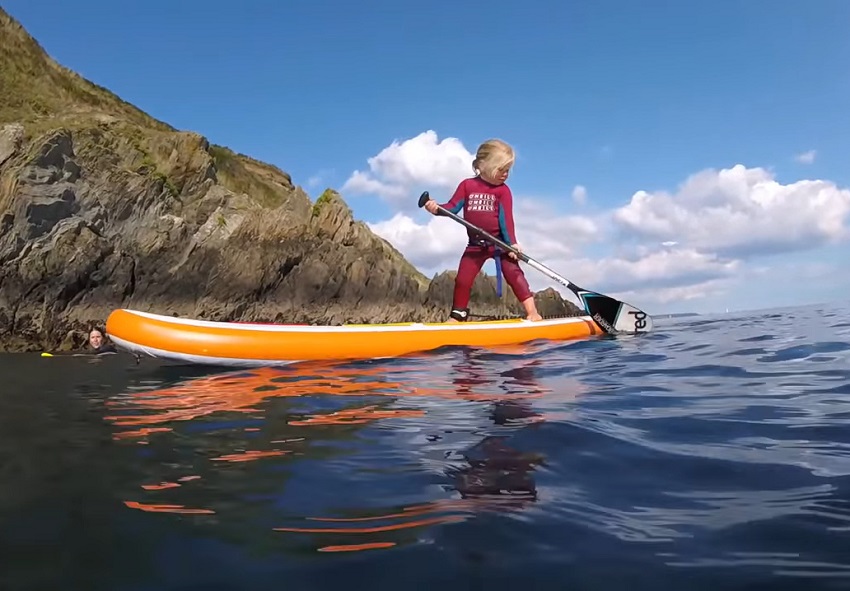 A girl paddles an orange paddle board