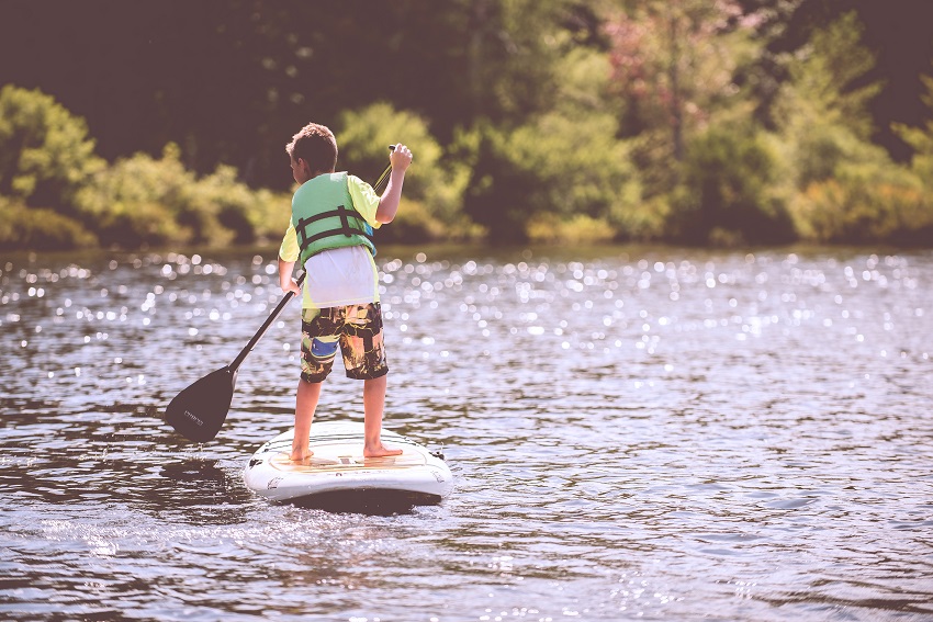 A boy in a green PFD paddles a stand up paddle board