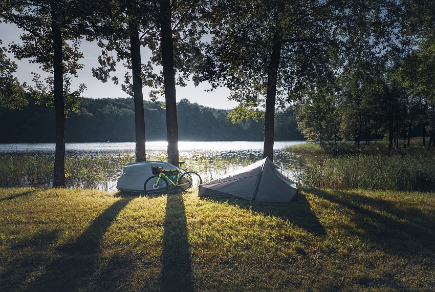 A one-person tent, a bike and a boat are on the lakeshore