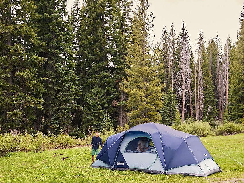 A man stands near the pitched Coleman Skydome 12-Person XL Tent in a forest