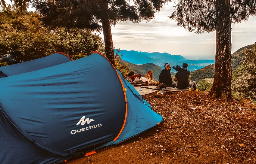 Three men sit on a mountain slope, two blue camping tents are pitched behind them