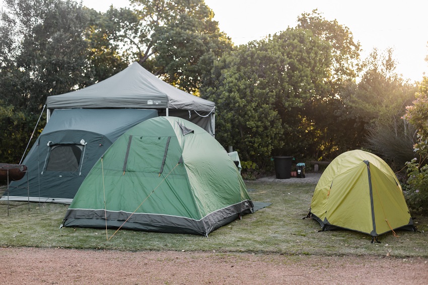 A small yellow tent, a medium-size green tent and big grey tent are pitched outdoors