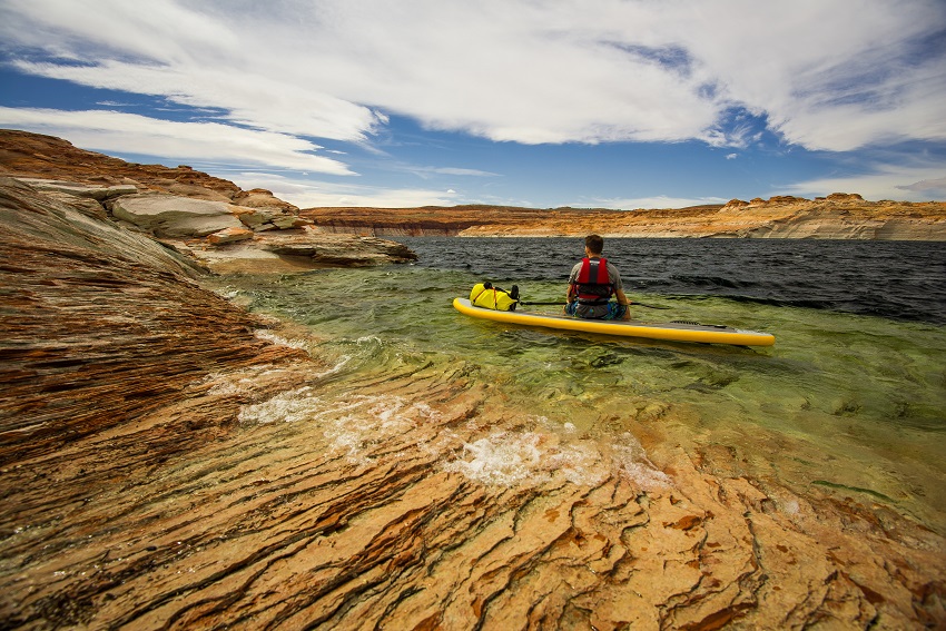 A man sits on a yellow touring paddle board on the stony shore
