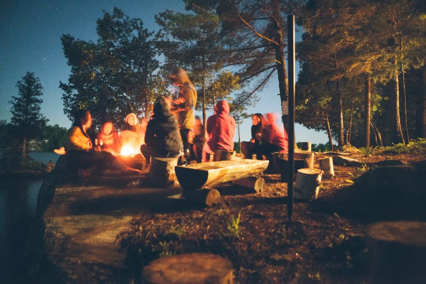 A group of people sits around a campfire in a forest at night