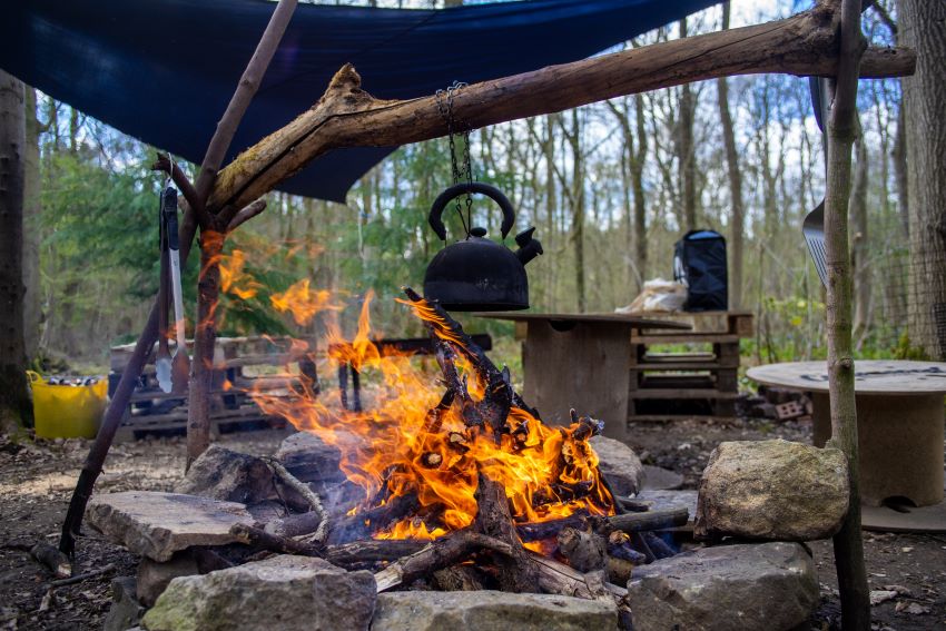 A teapot, suspended on a log, is heated over a campfire