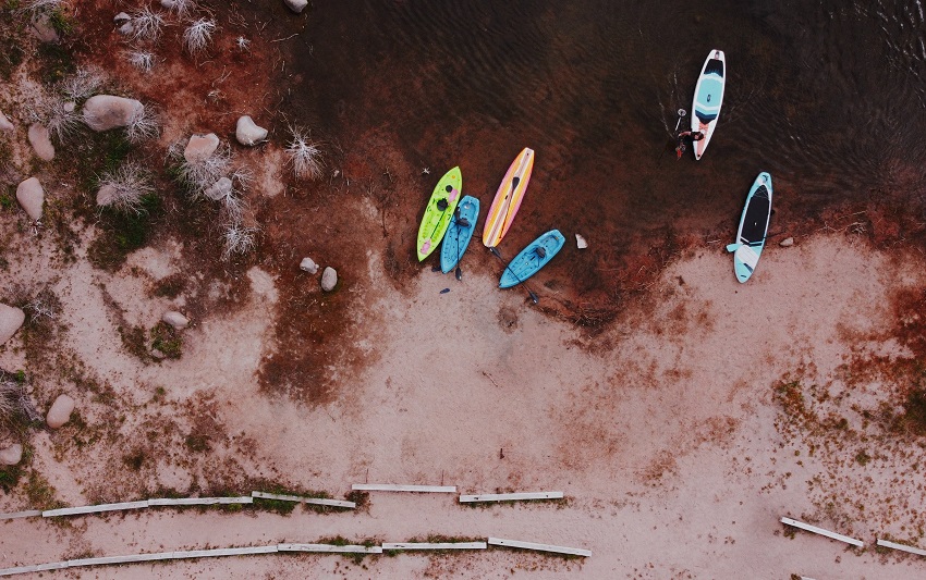 Different kayaks and SUPs are on a lake shore