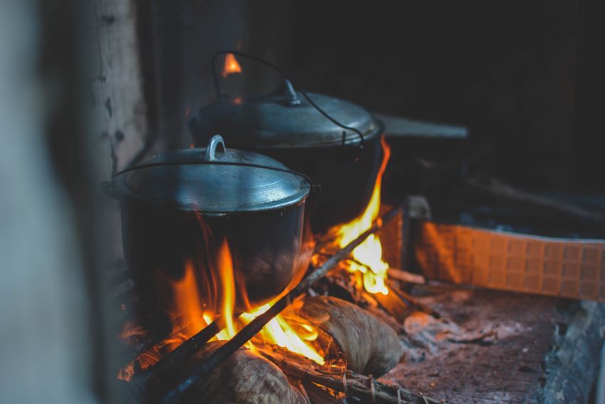 Two metal pots are heated over an open campfire