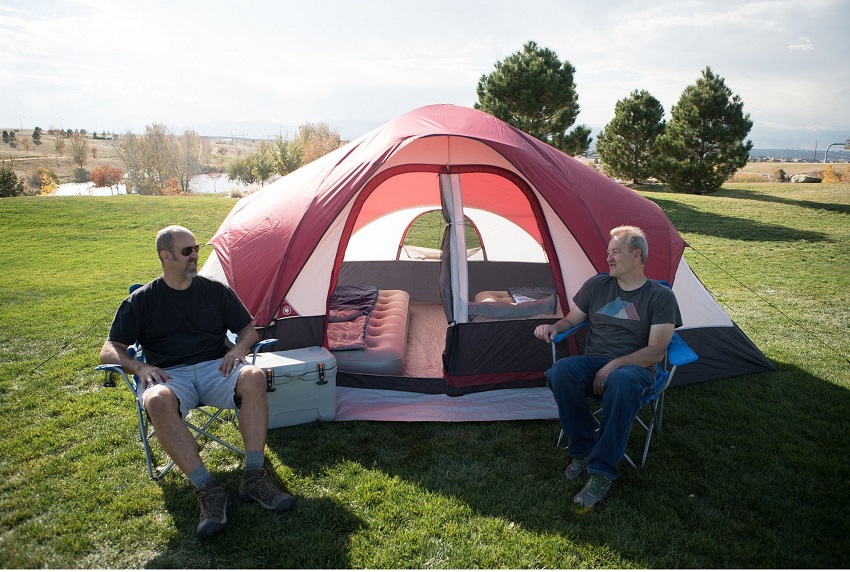 Two men talk to each other, sitting in camping chairs in front of the Ozark Trail 8-Person Dome tent