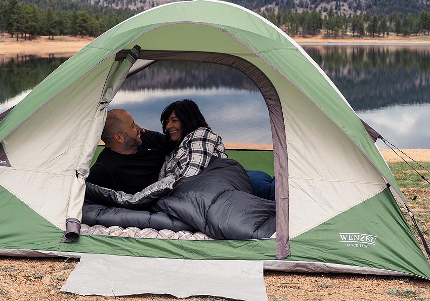 A man and a woman relax inside the Wenzel Jack Pine 4-Person Dome Tent, pitched near a lake
