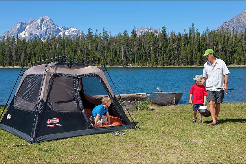 A man, holding a fishing rod, and his child look at another child in the Coleman 4-Person Cabin Camping Tent With Instant Setup