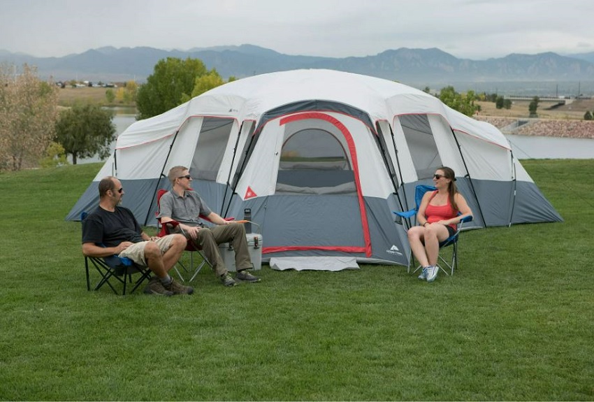 Two men and a woman sit in camping chairs near the Ozark Trail 20-Person 4-Room Cabin Tent