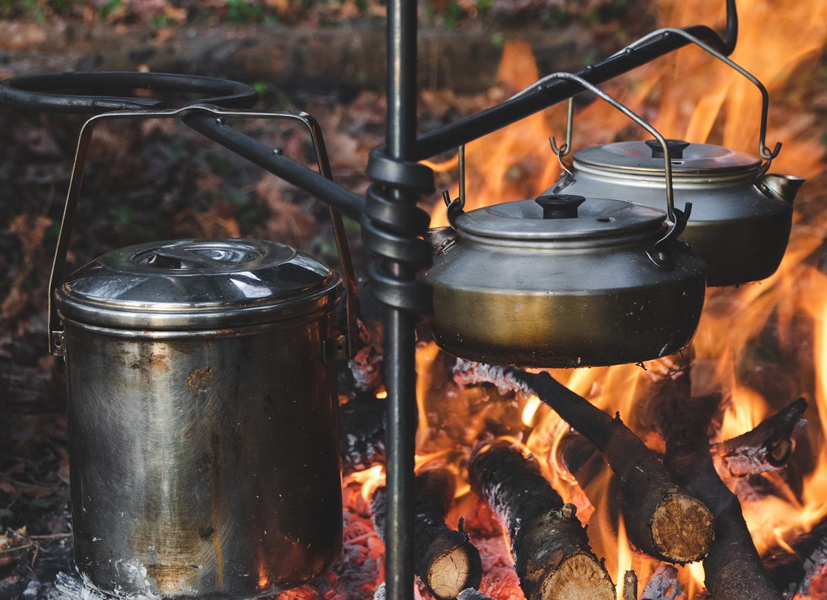 A pan with a lid and 2 teapots are heated over a campfire