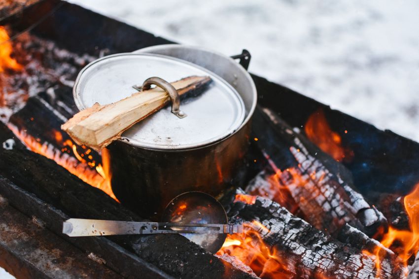 A pan with a lid is heated on a campfire