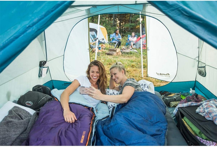 Two women in sleeping bags look at something in their smartphone inside the Eureka Space Camp 4 Person Tent