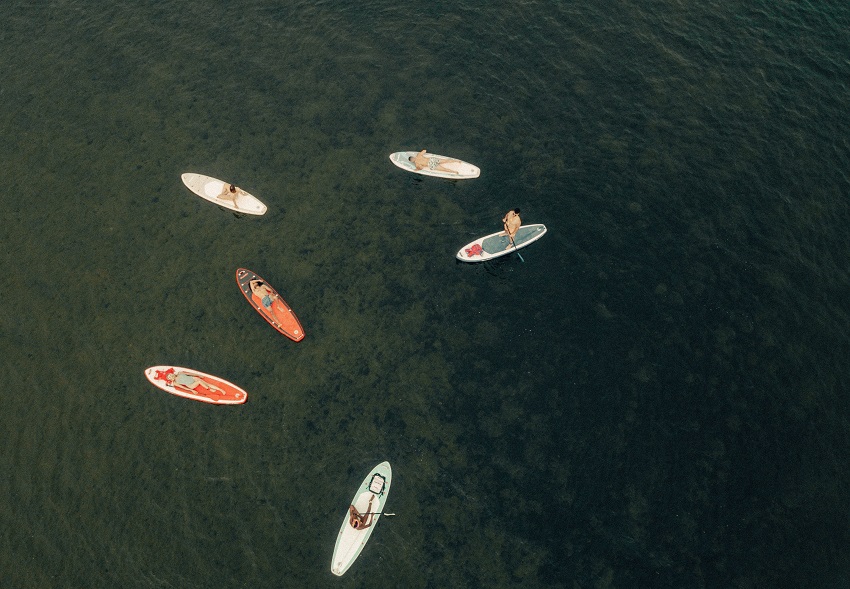Six different paddle boards with resting people float on water