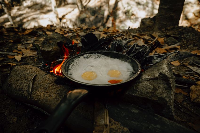 Two eggs are fried on a pan over a campfire
