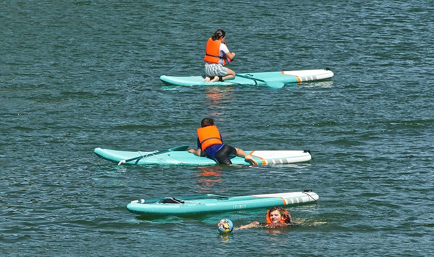 Three kids in orange PFDs spend time on their SUPs on open water
