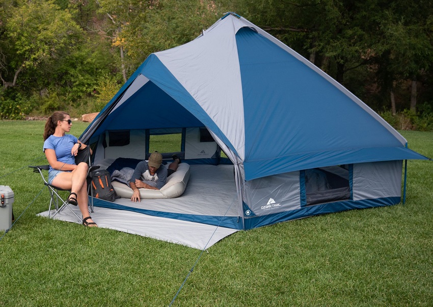 A woman sits in a chair and look at a man lying in the Ozark Trail Crystal Caverns 10-Person Festival Tent With 2 Entrances