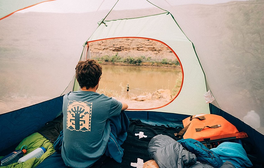 A man sits inside the Eureka Kohana 6-person tent and looks at a lonely angler, standing in the nearby river