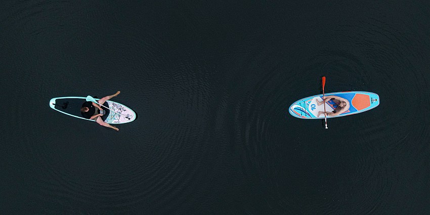 Two men sit on their paddle boards, facing each other