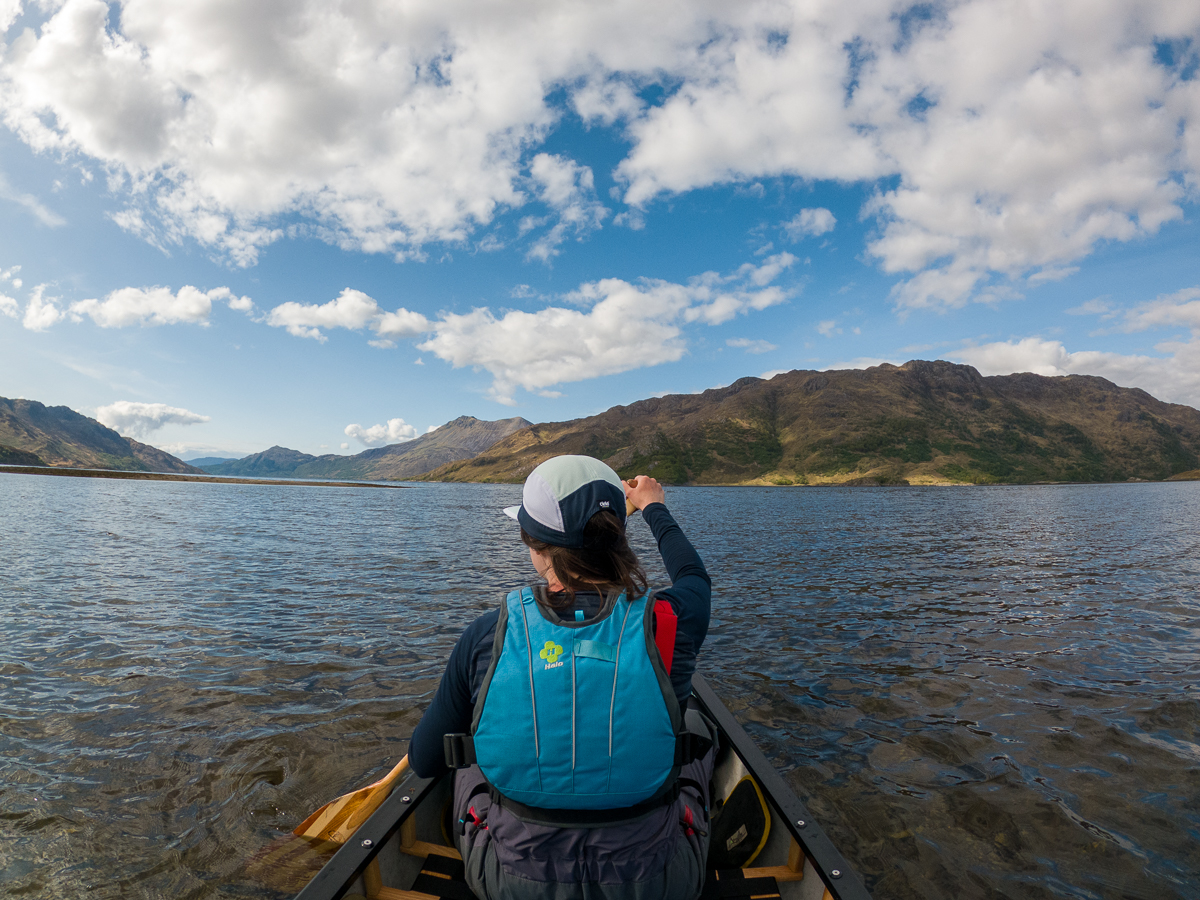 A woman wearing a blue life vest paddles her canoe on a lake