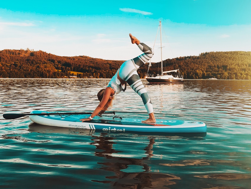 A woman practices yoga, standing on her hands and one leg on a SUP
