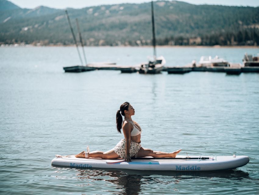 A woman practices yoga, sitting on a twine on a SUP