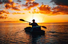 An angler paddles his fishing kayak at sunset