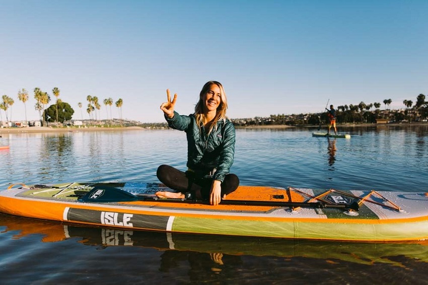 A woman sits on an orange ISLE SUP on the water