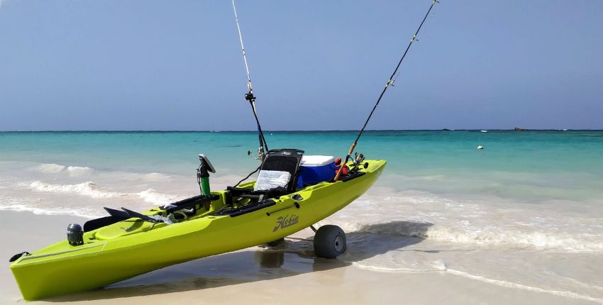 A yellow fishing kayak with two fishing rods on the beach