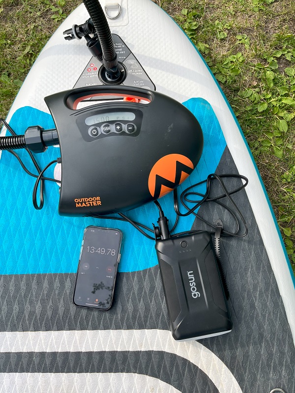 OutdoorMaster Shark II SUP pump is connected to a power bank and an inflatable paddle board