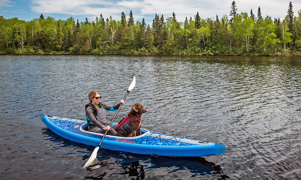 A woman with her dog paddles a blue inflatable kayak