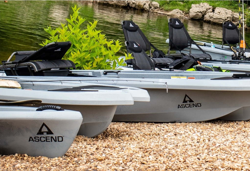Several grey Ascend kayaks are stored onshore