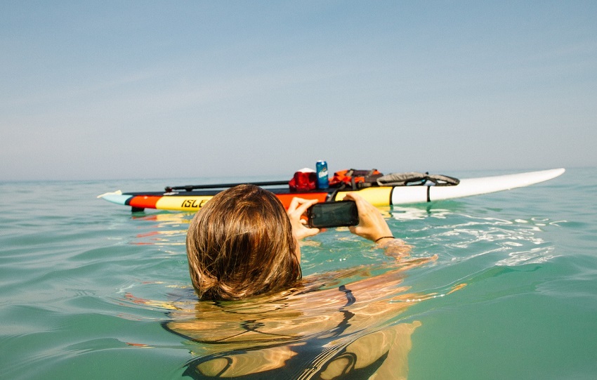 A woman takes a picture of her SUP with gear, while sitting in the water