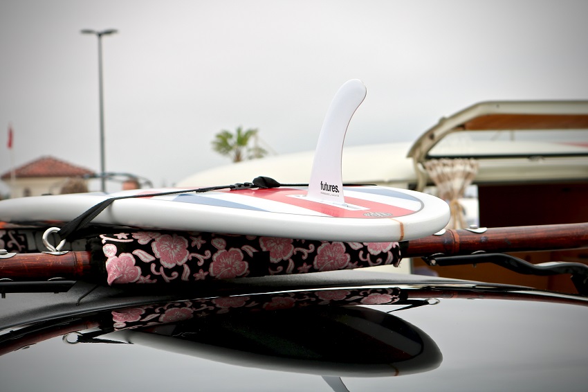 A hard-shell SUP is attached to a car roof rack