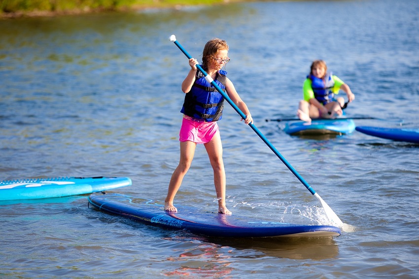 A girl in a blue PFD paddles a blue SUP on water