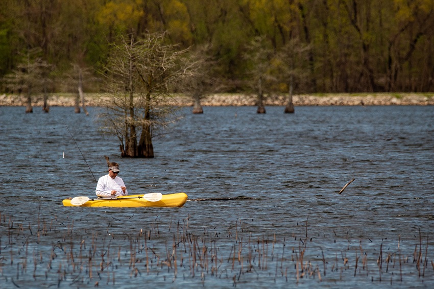 A man sits in a yellow sit-in fishing kayak on a lake