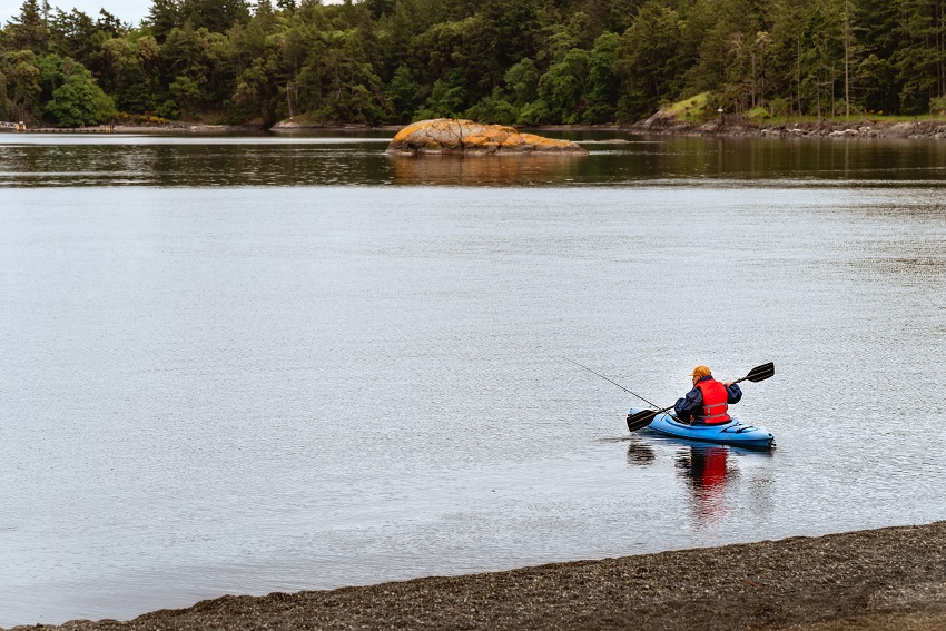 An angler paddles his blue sit-in kayak on a lake